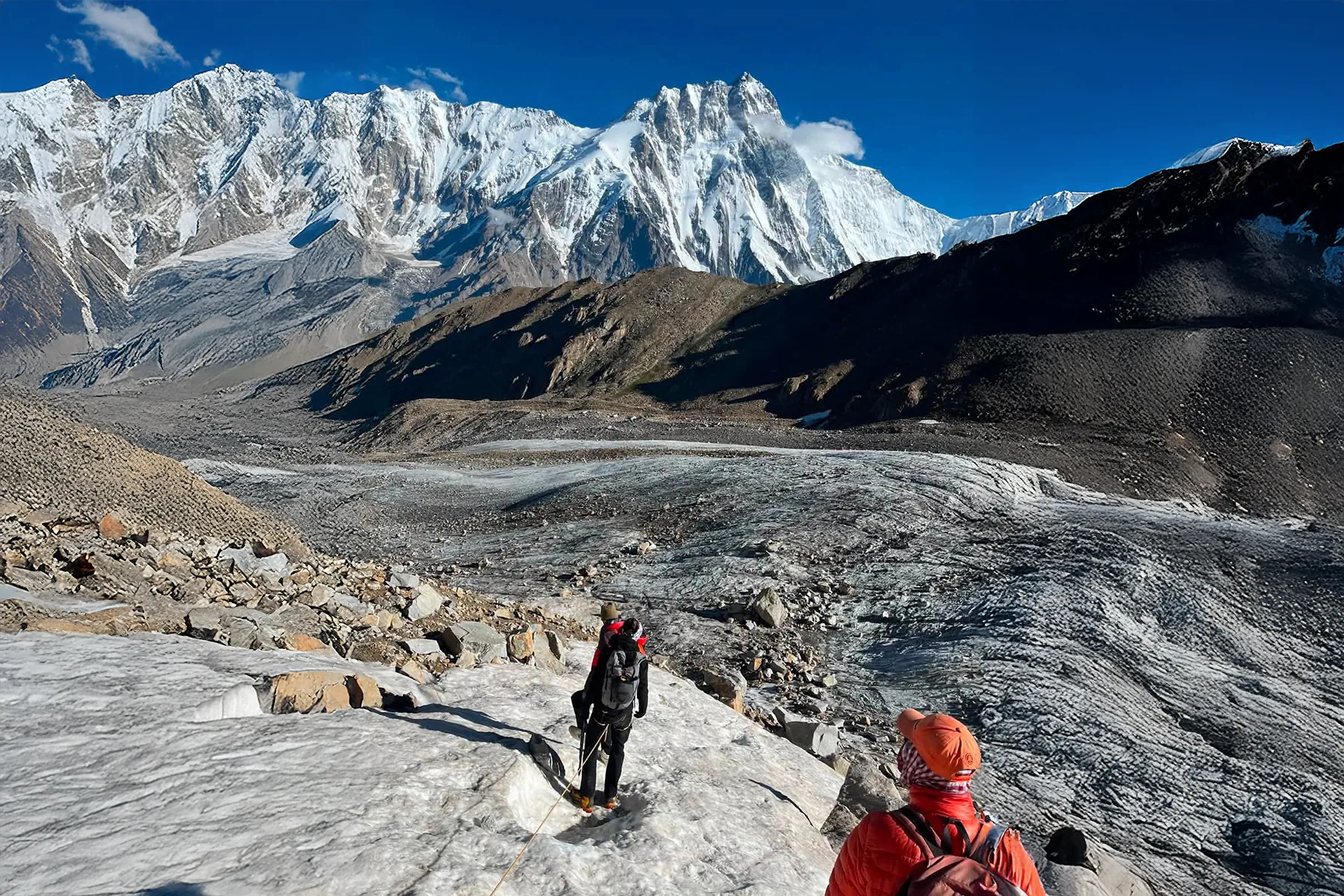 Rope team of trekkers on a glacier below a giant Karakoram peak
